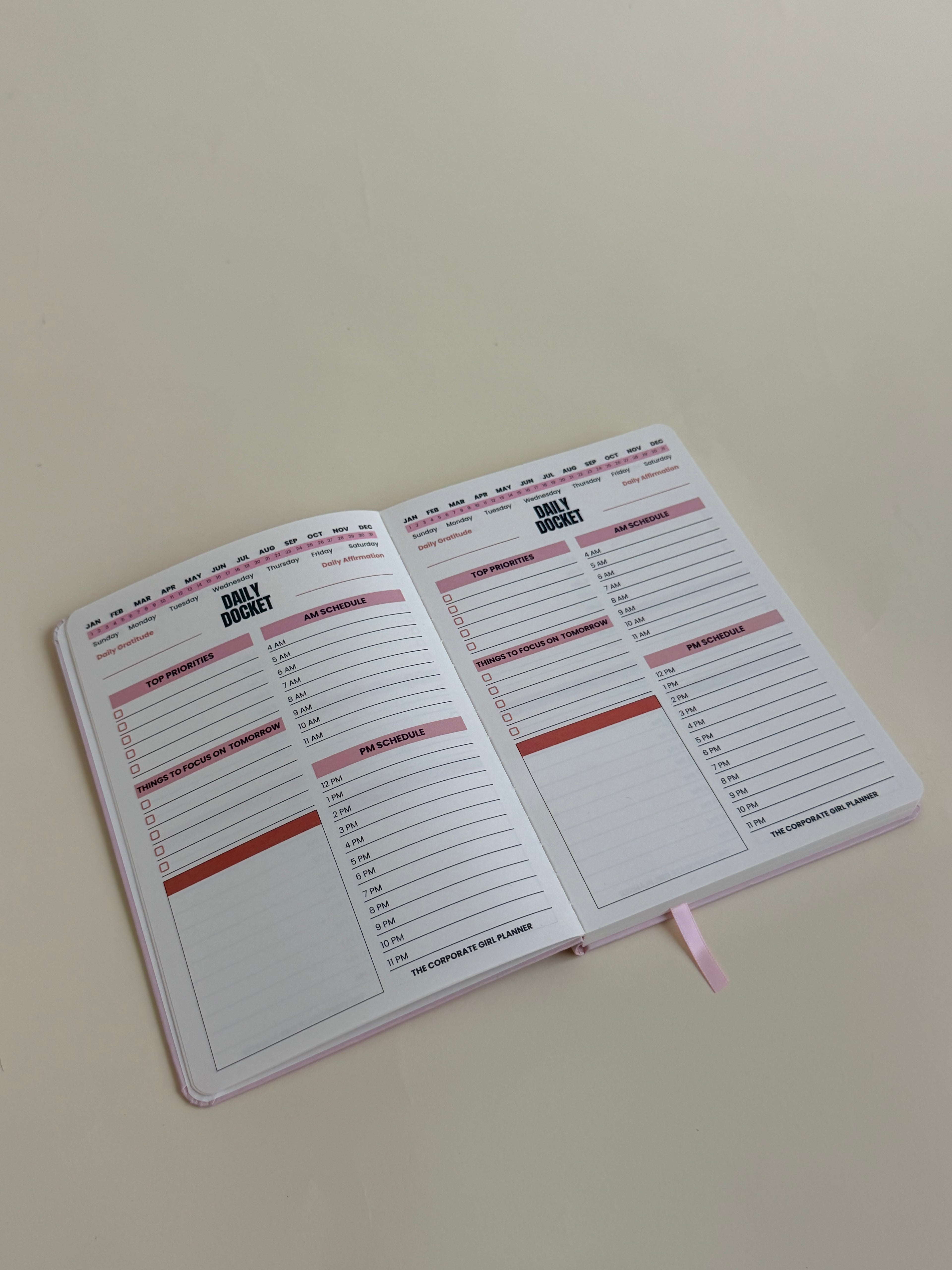 An open Daily Docket planner with lined pages, pink headers, and a pink ribbon bookmark, photographed on a plain light beige background.