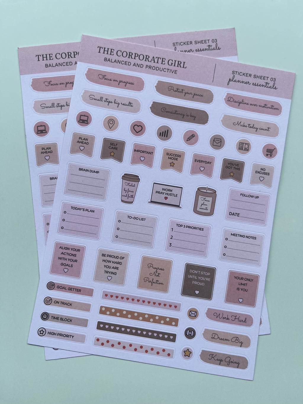 Three planner sticker sheets titled 'The Corporate Girl' arranged diagonally on a light mint green background. The stickers feature neutral tones of beige, taupe, and dusty pink with various icons, labels, and motivational phrases for productivity.
