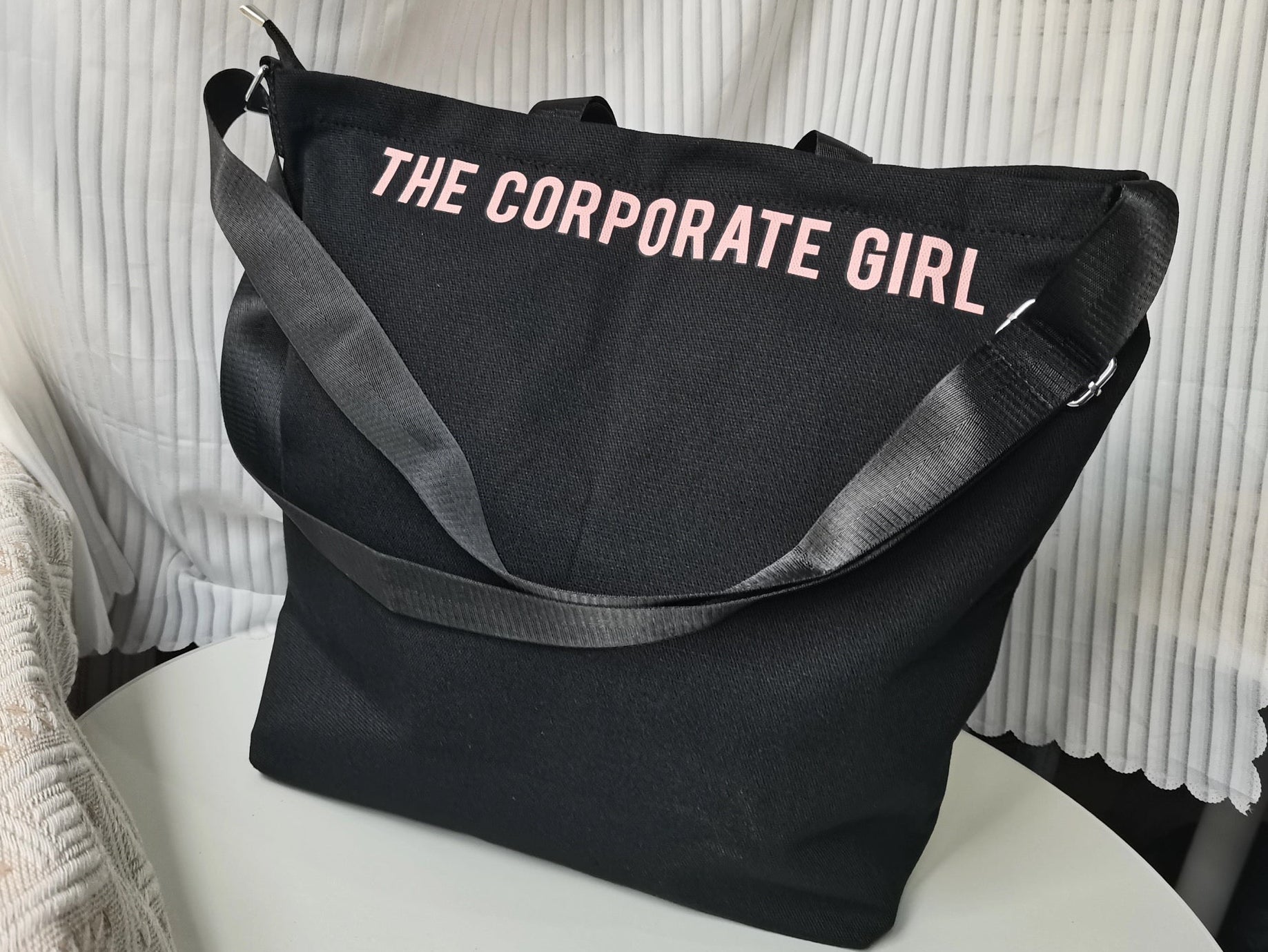 Black tote bag with 'THE CORPORATE GIRL' text on a white surface